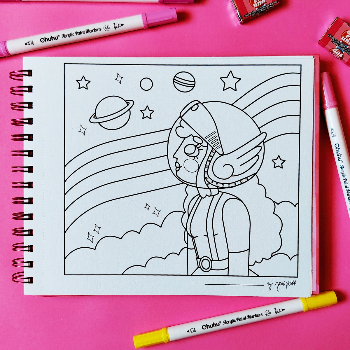 Libro Chicle Rosa abierto con una ilustración para colorear de una niña astronauta, planetas, estrellas y arcoíris sobre fondo rosa.