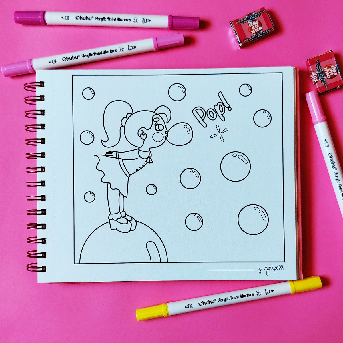 Libro Chicle Rosa abierto con una niña soplando chicle, burbujas y la palabra «Pop!», rodeado de marcadores sobre fondo rosa.