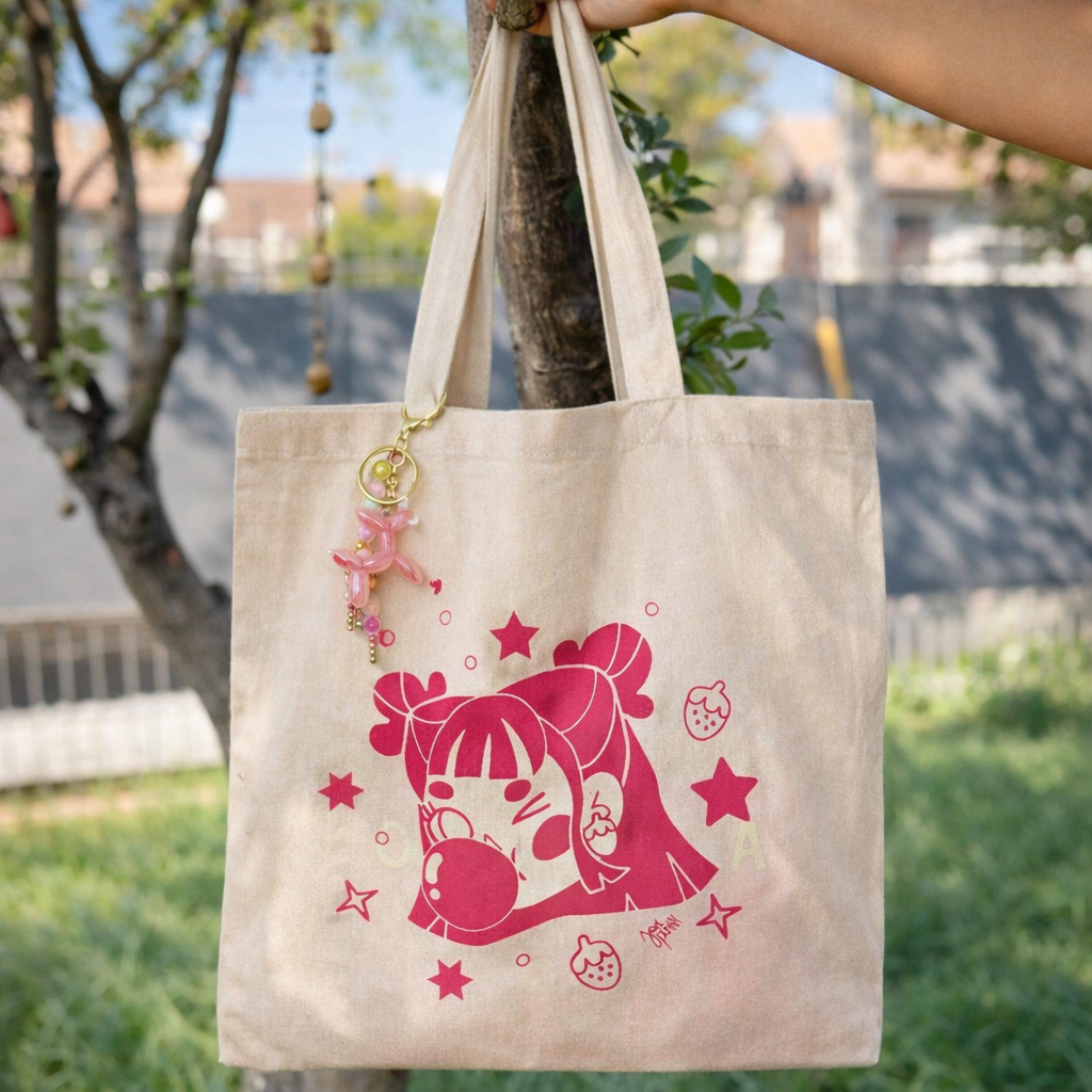 Totebag beige Chicle Rosa de Javipinkk con ilustración fucsia y llavero rosado, sostenida al aire libre junto a un árbol.